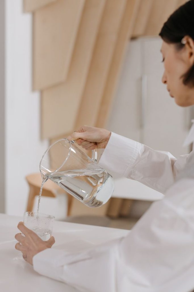 Crafting Captivating Headlines: Your awesome post title goes here Woman in white shirt pouring water from a pitcher into a glass in a modern indoor setting.