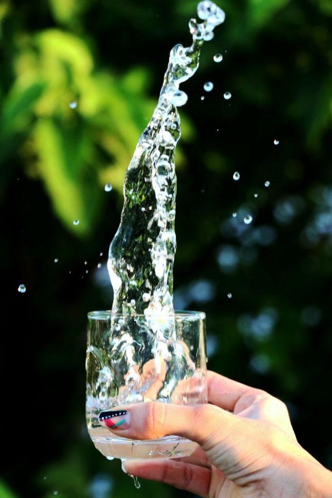 A dynamic shot of water splashing from a glass held by a hand against a leafy green background.
